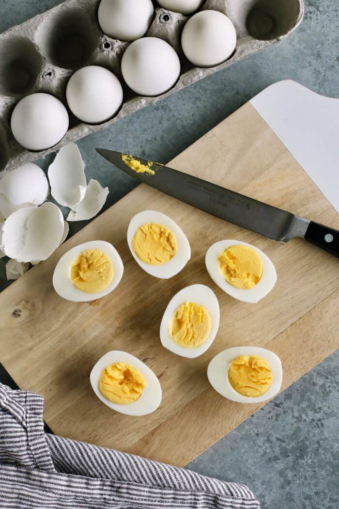 Peeled hard boiled eggs are cut in half on a cutting board.