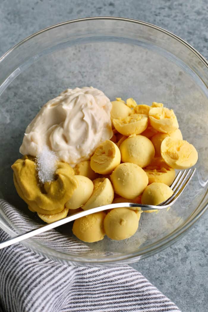 The hard boiled egg yolks are combined with mayonnaise, mustard, salt, and vinegar in a glass bowl.