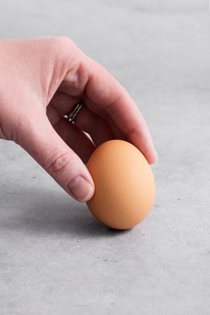 a hand holding an egg to show which end of the egg to tap, to start peeling off the shell