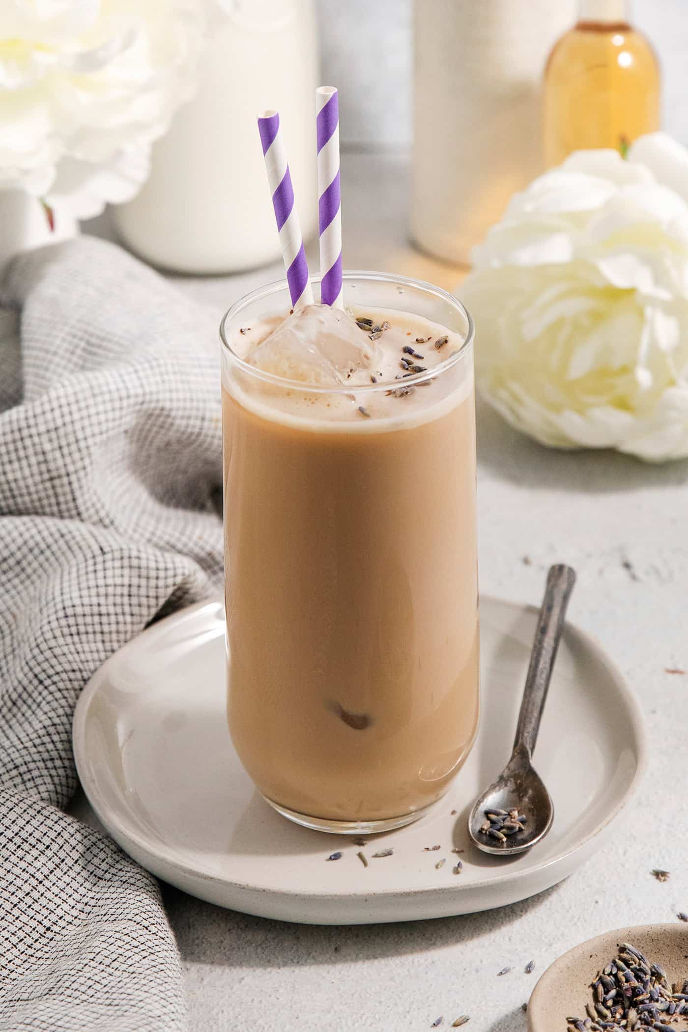 A glass of lavender latte on a plate with a spoon.