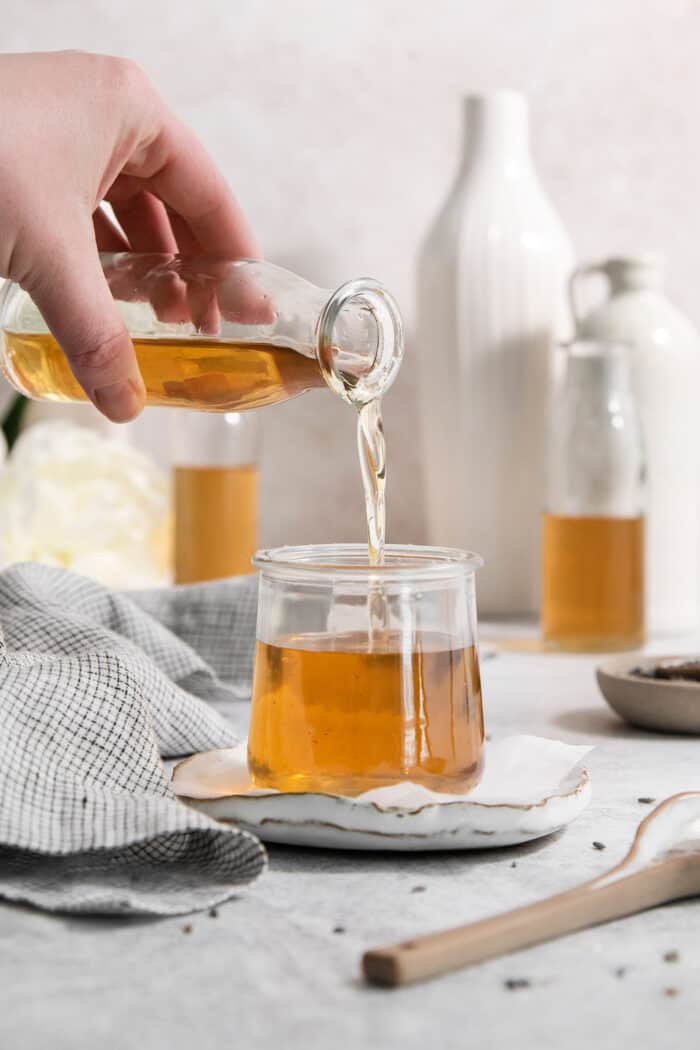 A hand pours lavender simple syrup from a bottle into a jar.