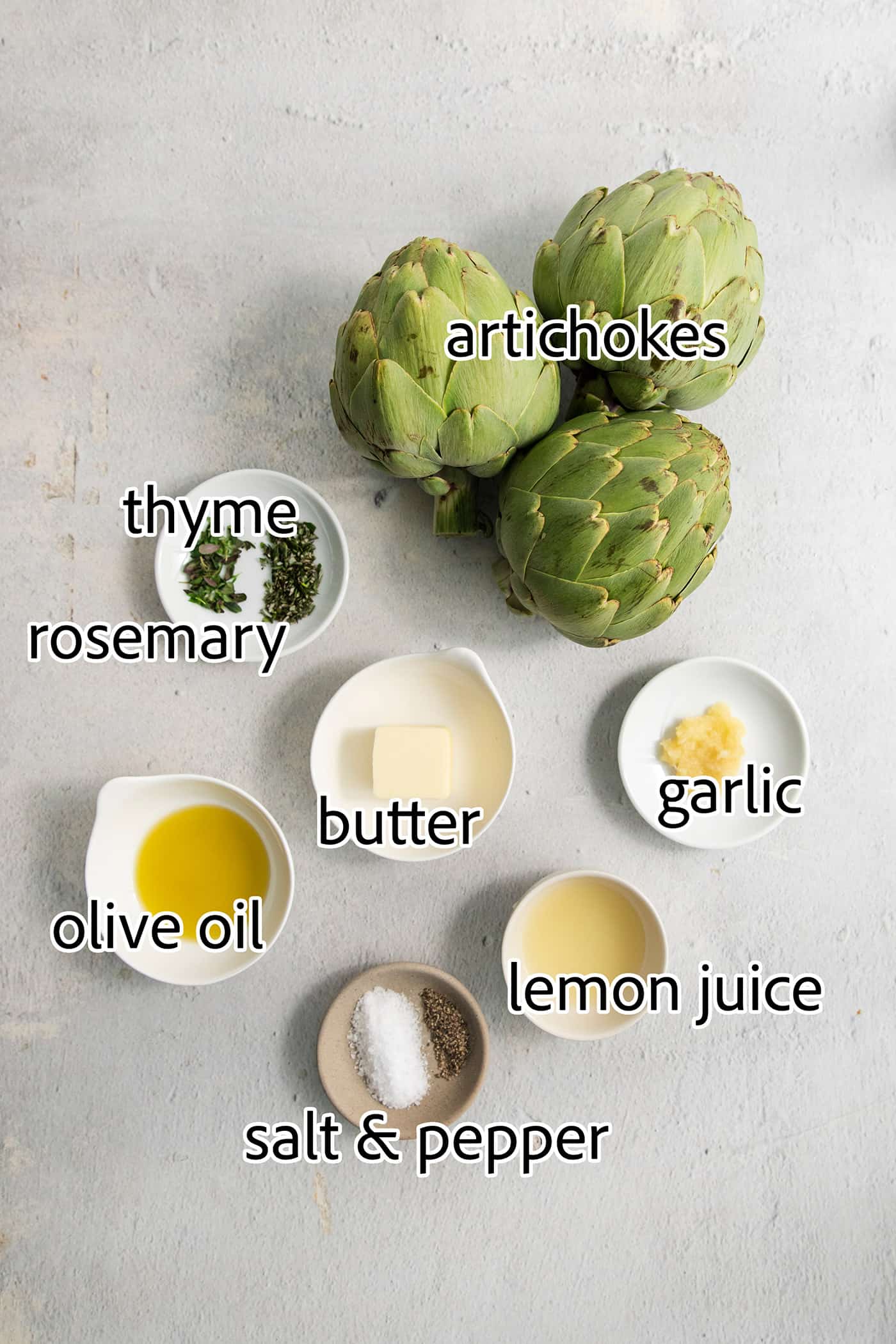 The ingredients needed for roasted artichoke are shown: three raw artichokes, olive oil, salt, butter, rosemary, thyme, lemon juice, and garlic.
