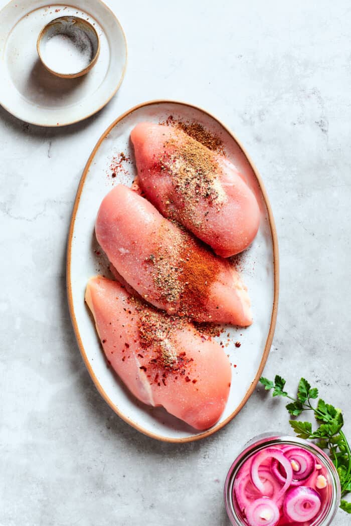 Three chicken breasts are seasoned on a plate.