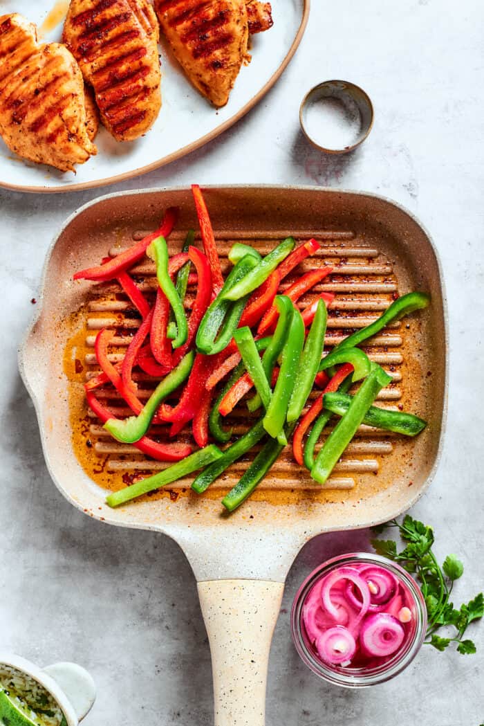 Red and green bell pepper slices cook on a grill.