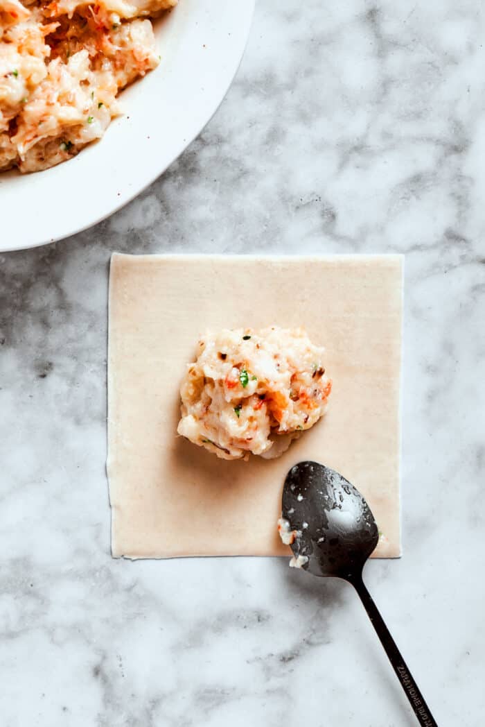 The shrimp filling is added to the wonton wrapper.