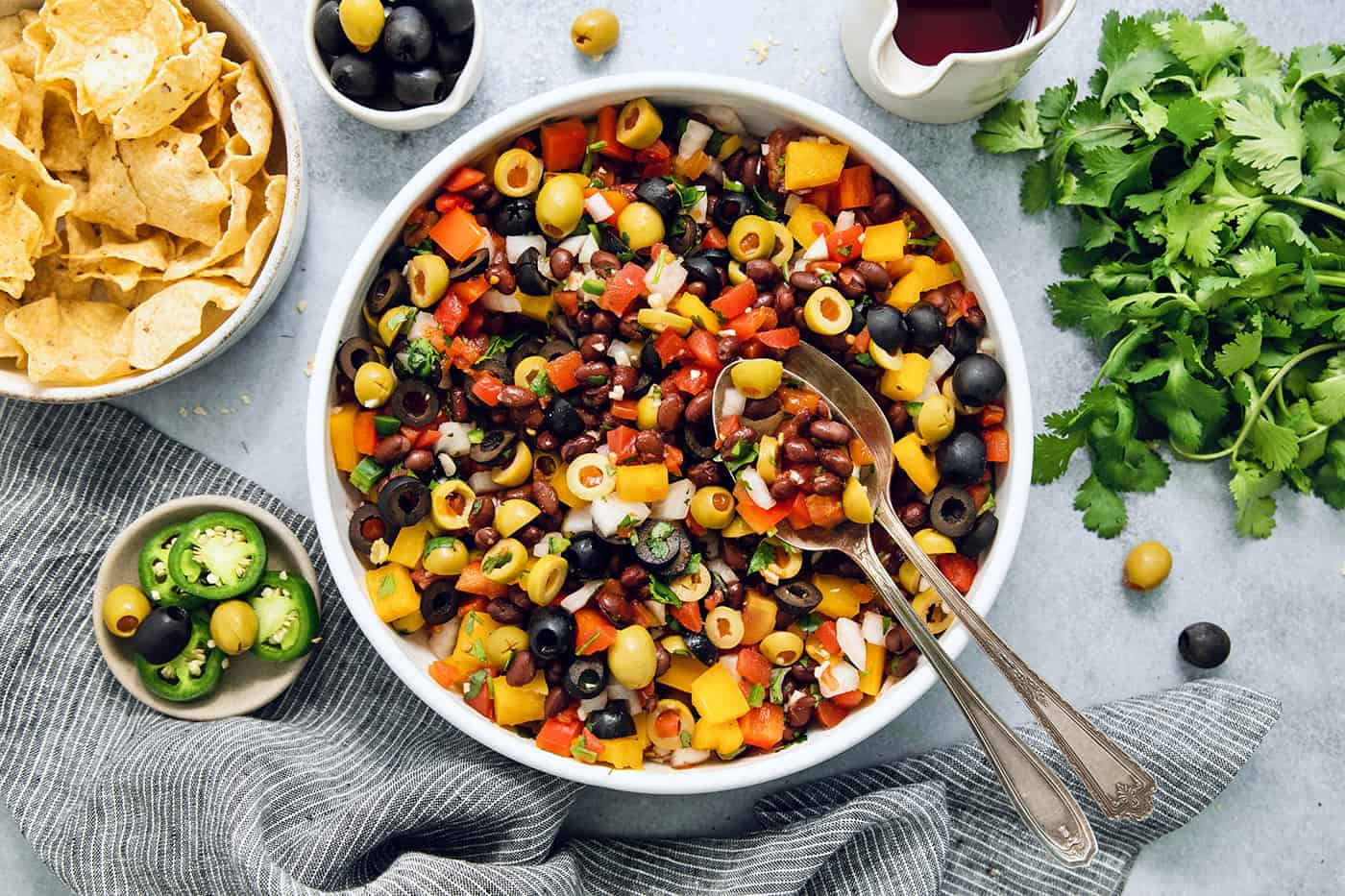 Serving utensils rest in a big bowl of black bean salsa.