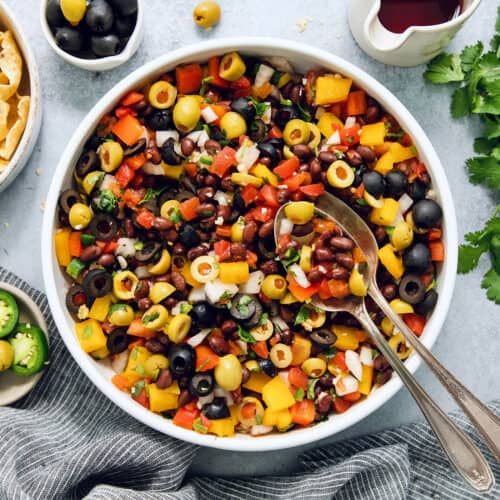 Serving utensils rest in a big bowl of black bean salsa.