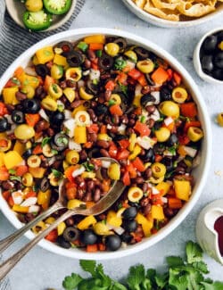 Serving utensils rest in a big bowl of black bean salsa.