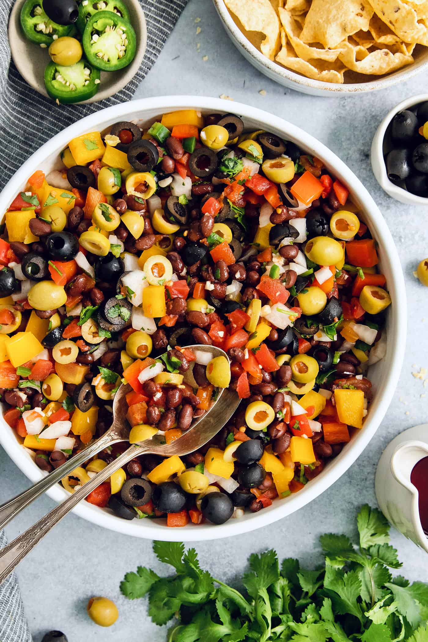 Serving utensils rest in a big bowl of black bean salsa.