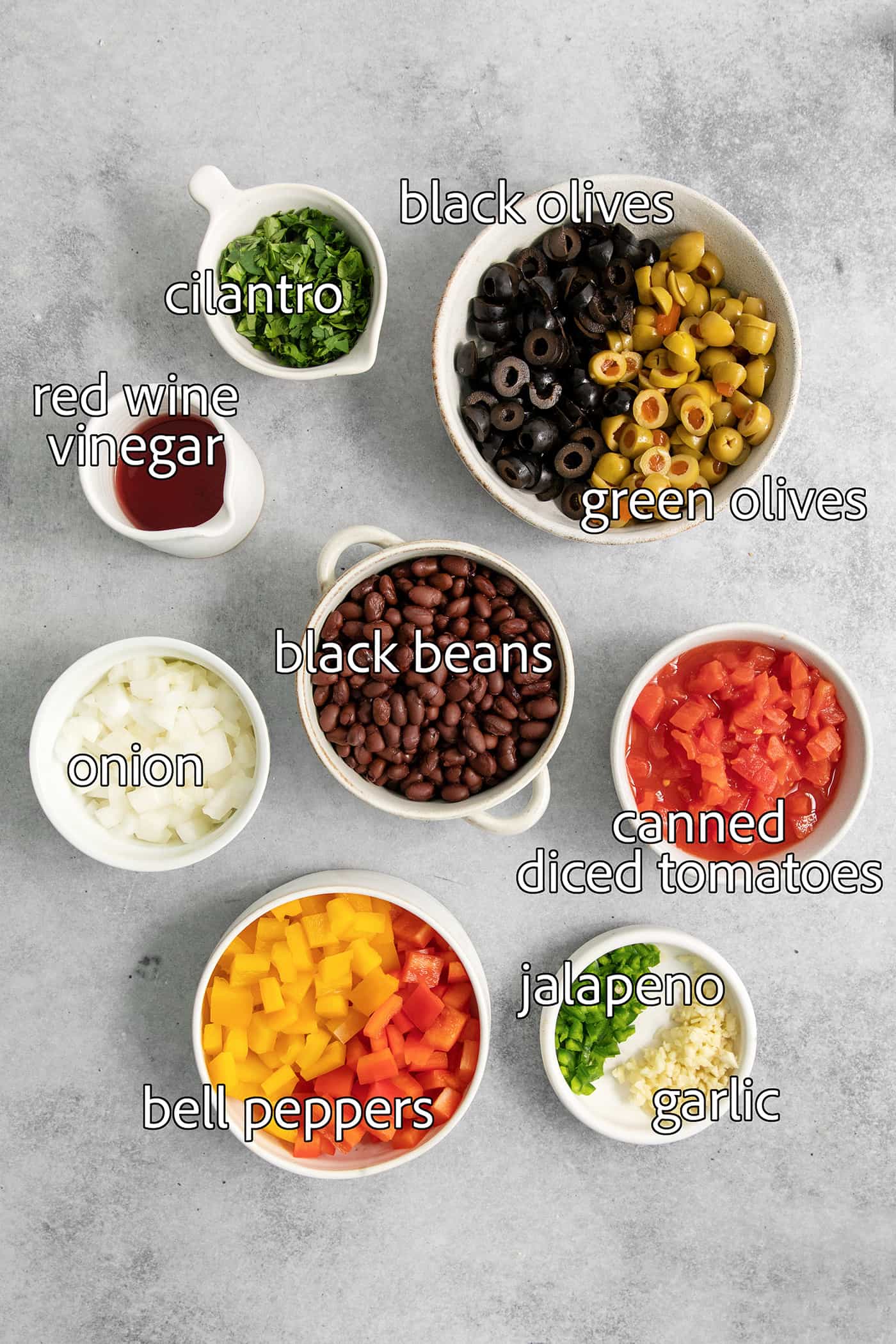 Ingredients for black bean salsa are portioned out and labeled: black beans, olives, onion, vinegar, cilantro, canned tomatoes, garlic, cilantro.