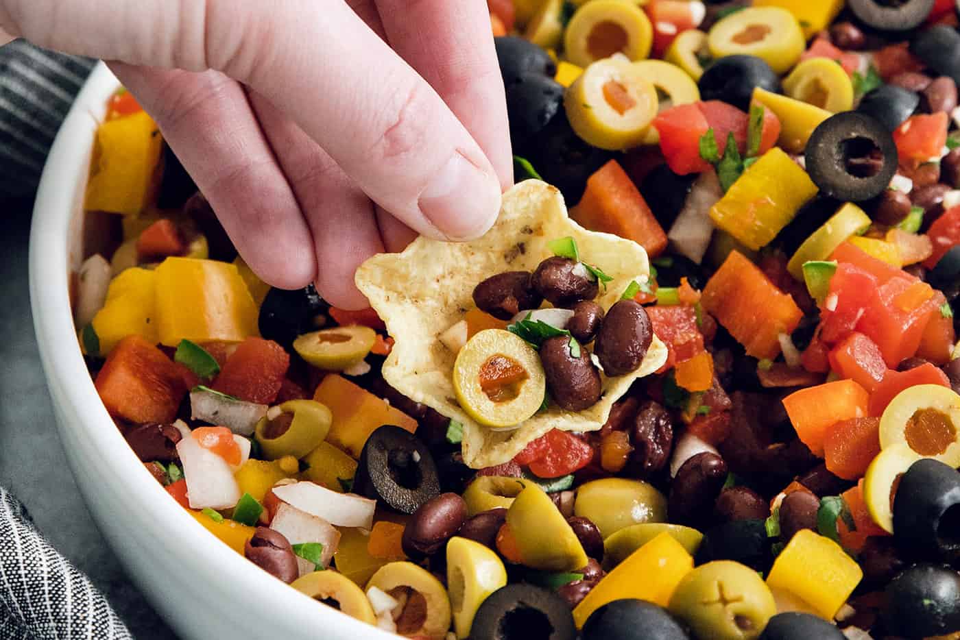 A hand holds a tortilla chip filled with black bean salsa.