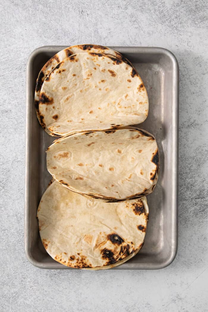 Charred tortillas are placed on a metal baking pan.