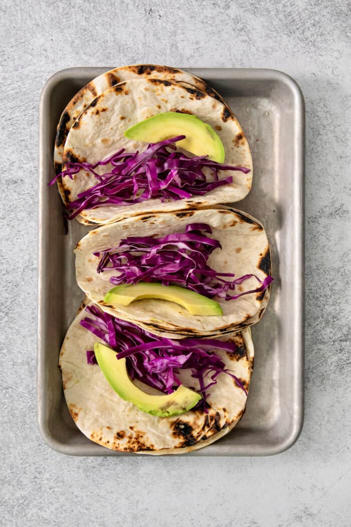 Avocado and red cabbage are added to the tortillas