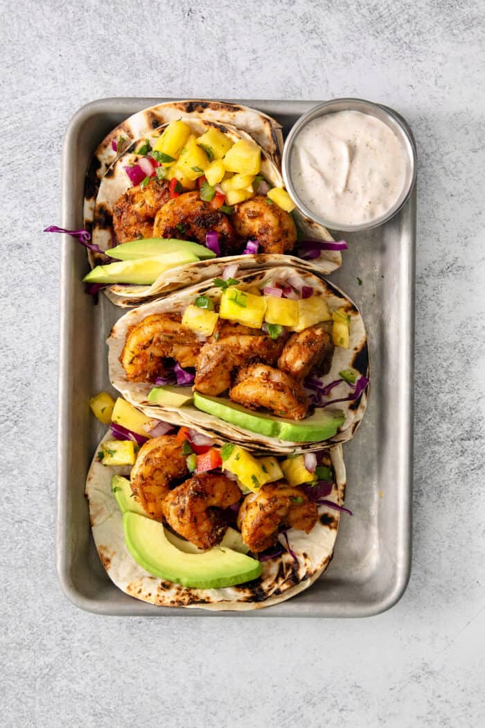 A tray of blackened shrimp tacos stuffed with shrimp, pineapple salsa, avocado, and cabbage.