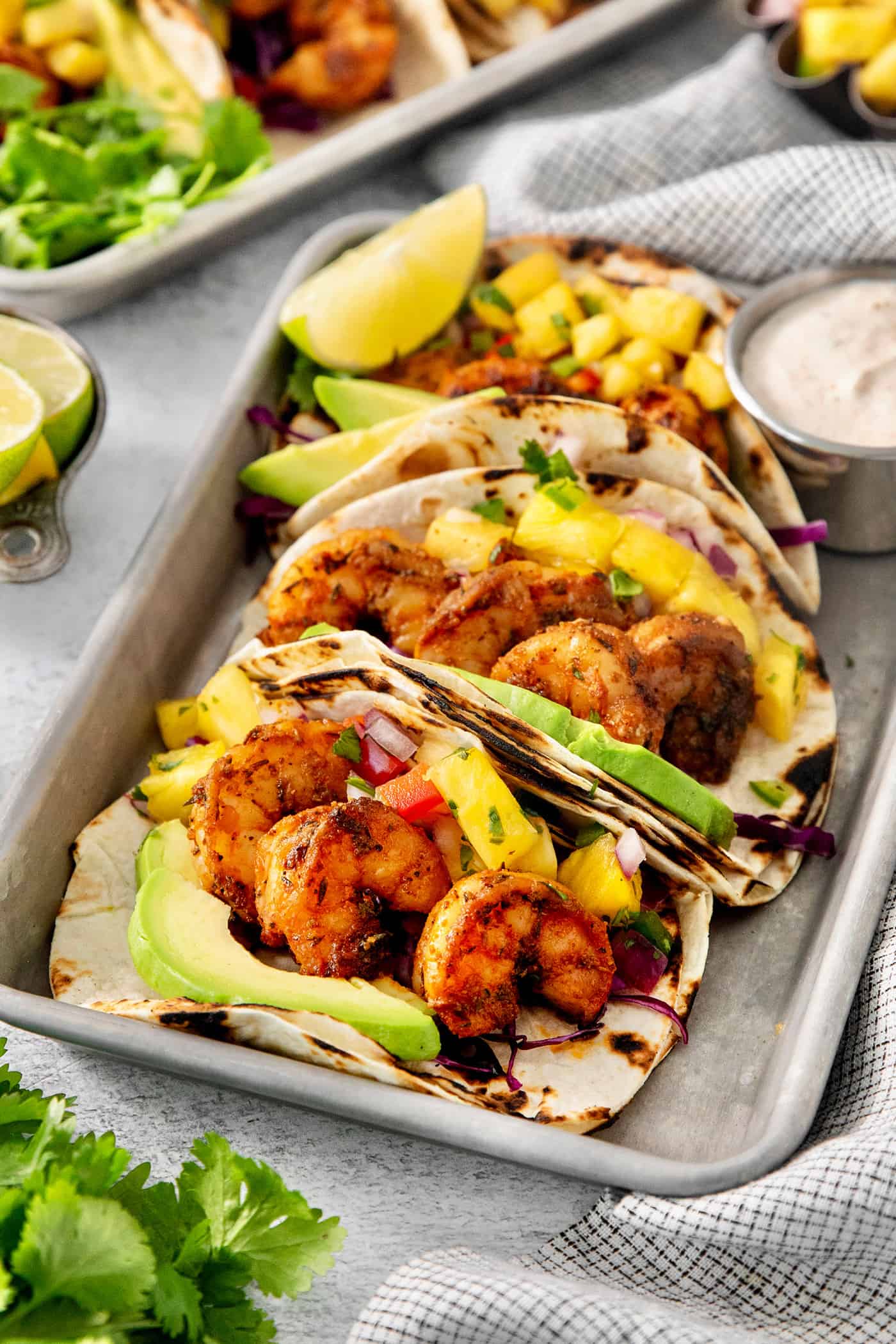 Trays of blackened shrimp tacos with lime wedges and avocado crema.