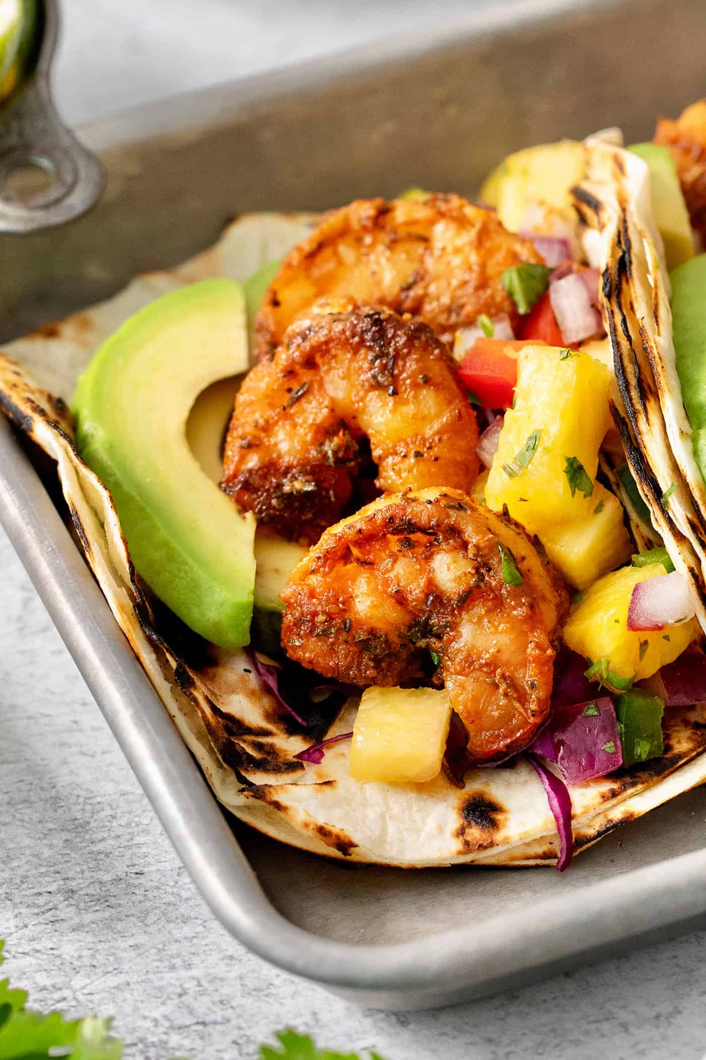 A charred flour tortilla is opened to show blackened shrimp, an avocado slice, and pineapple salsa.