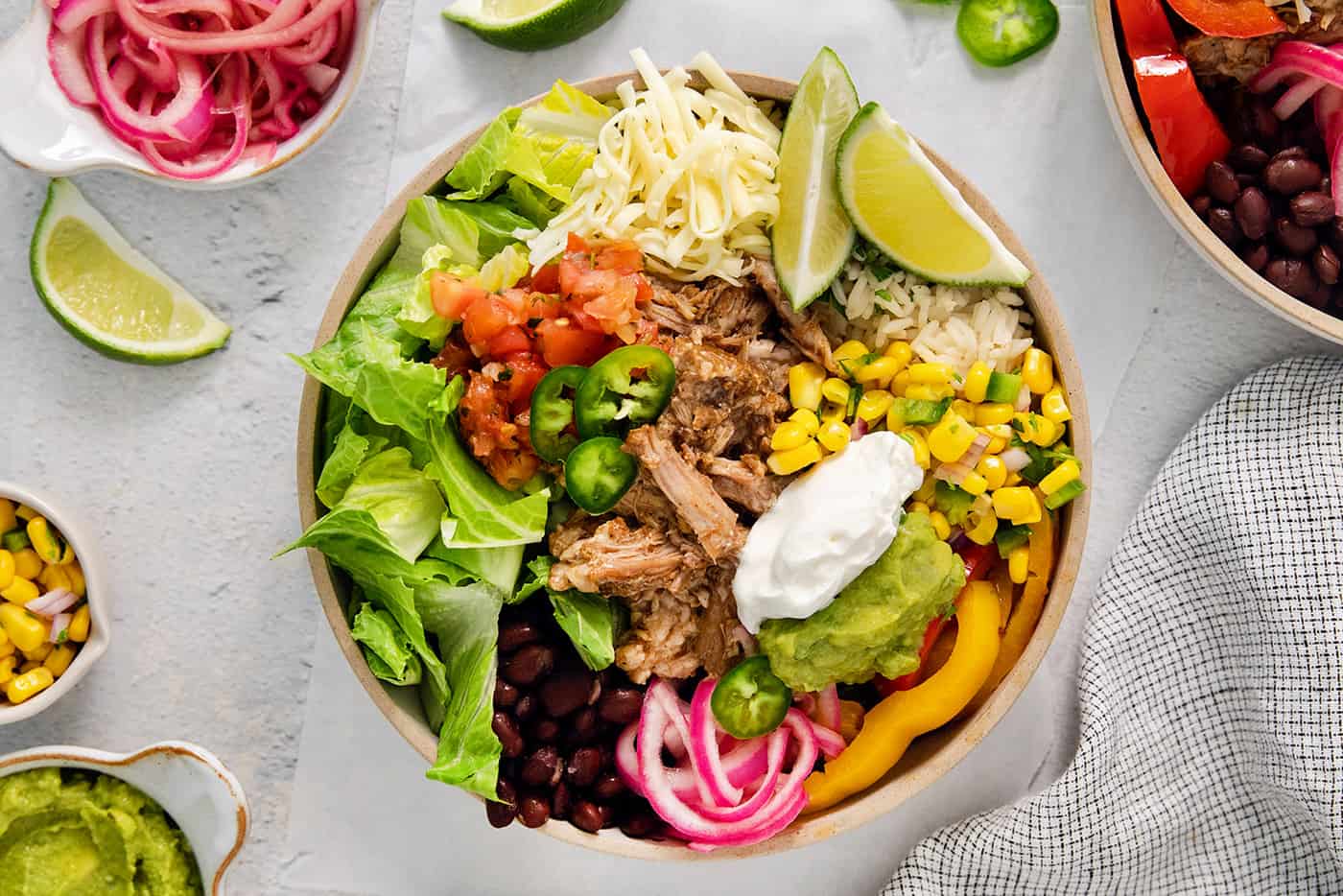 A colorful carnitas burrito bowl surrounded by toppings.