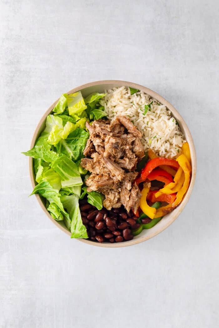 The ingredients are layered into a bowl for carnitas bowls.