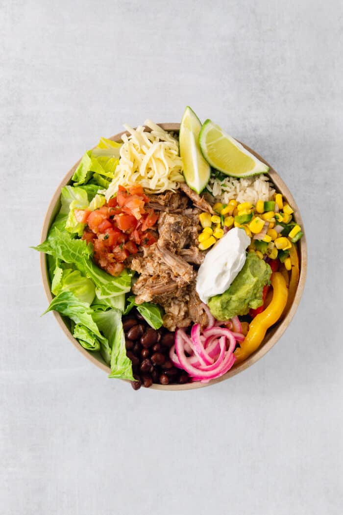 The salsas, guacamole, and sour cream are added to the top of the carnitas burrito bowl.