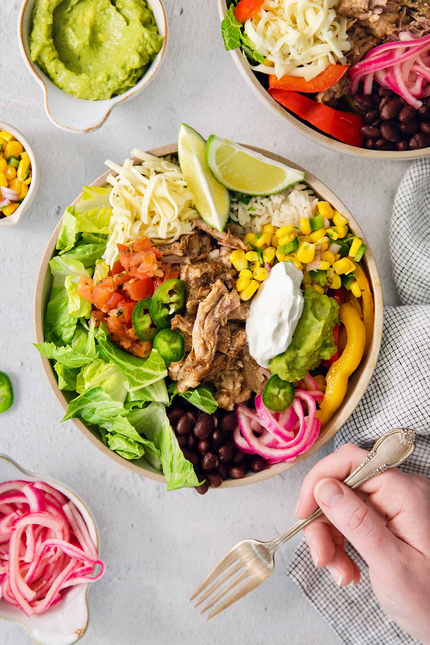 A carnitas burrito bowl topped with lime guacamole, and sour cream is ready to eat.