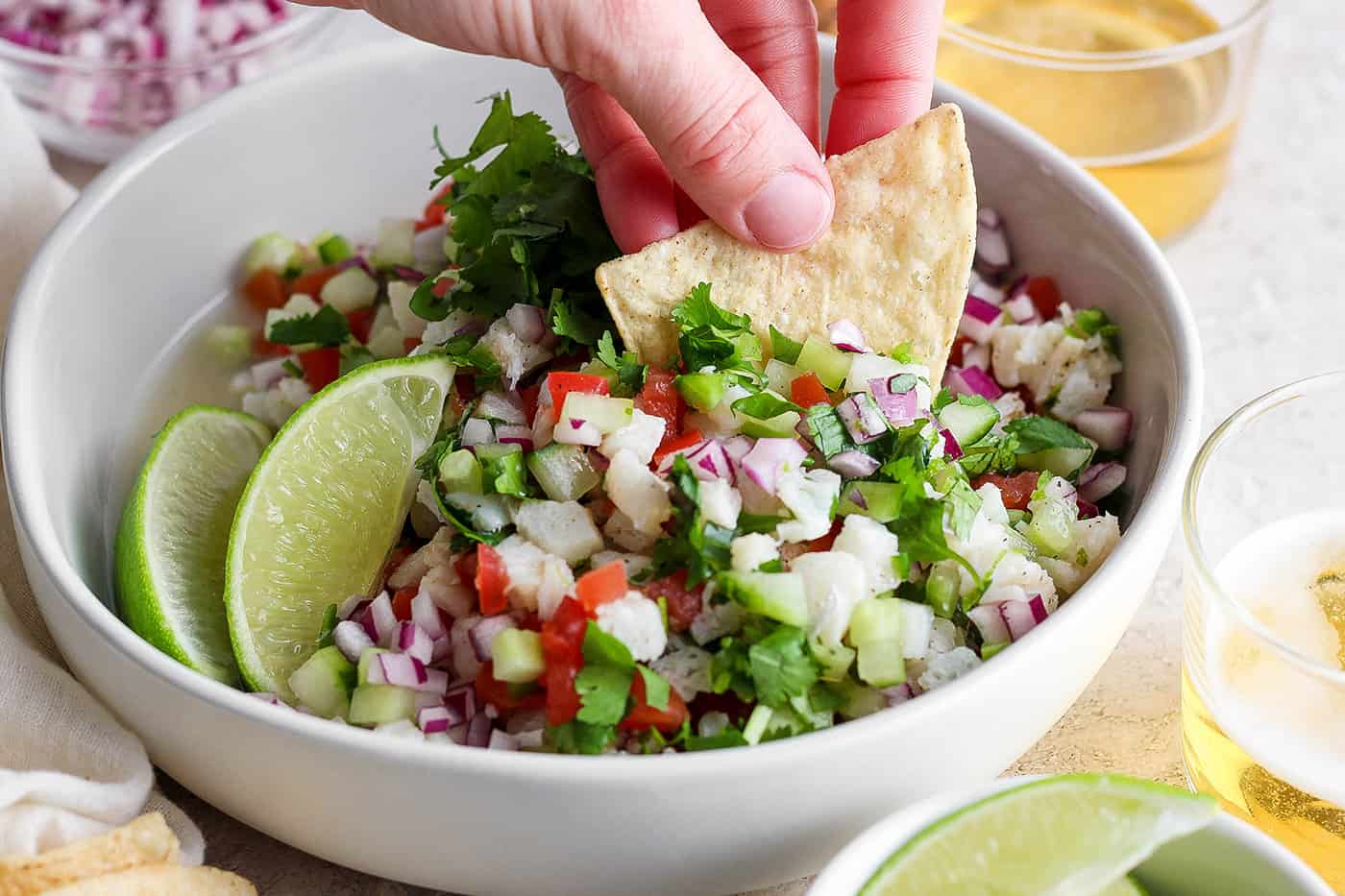 A hand dips a tortilla chip into a bowl of classic ceviche.