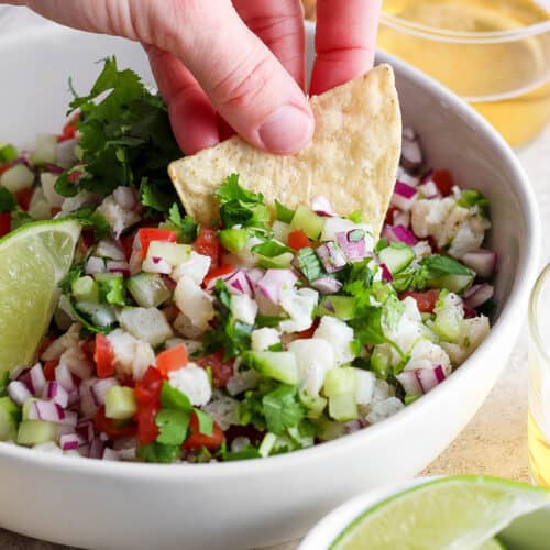 A hand dips a tortilla chip into a bowl of classic ceviche.