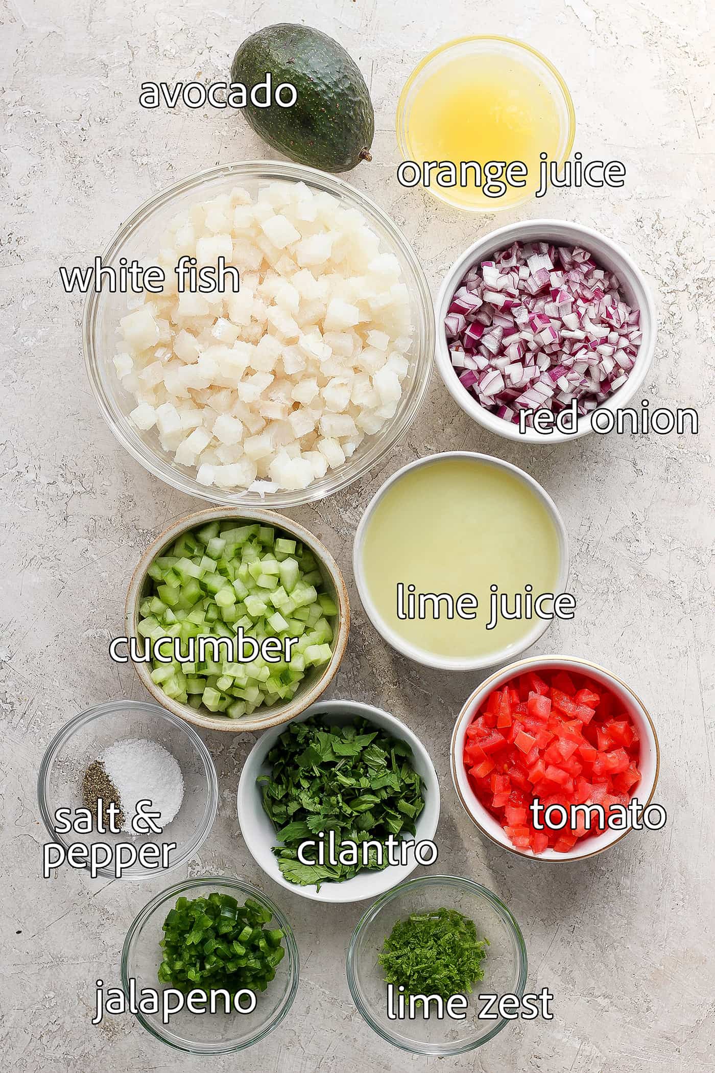 The ingredients for classic ceviche are shown portioned out and labeled: white fish, lime juice, orange juice, tomato, red onion, cilantro, salt and pepper, cucumber, avocado.