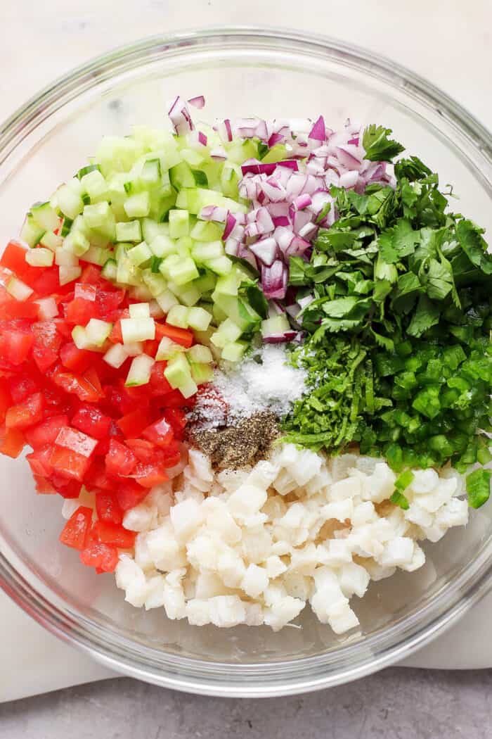 Vegetables are added to the bowl of ceviche.