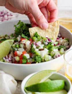 A hand dips a tortilla chip into a bowl of classic ceviche.