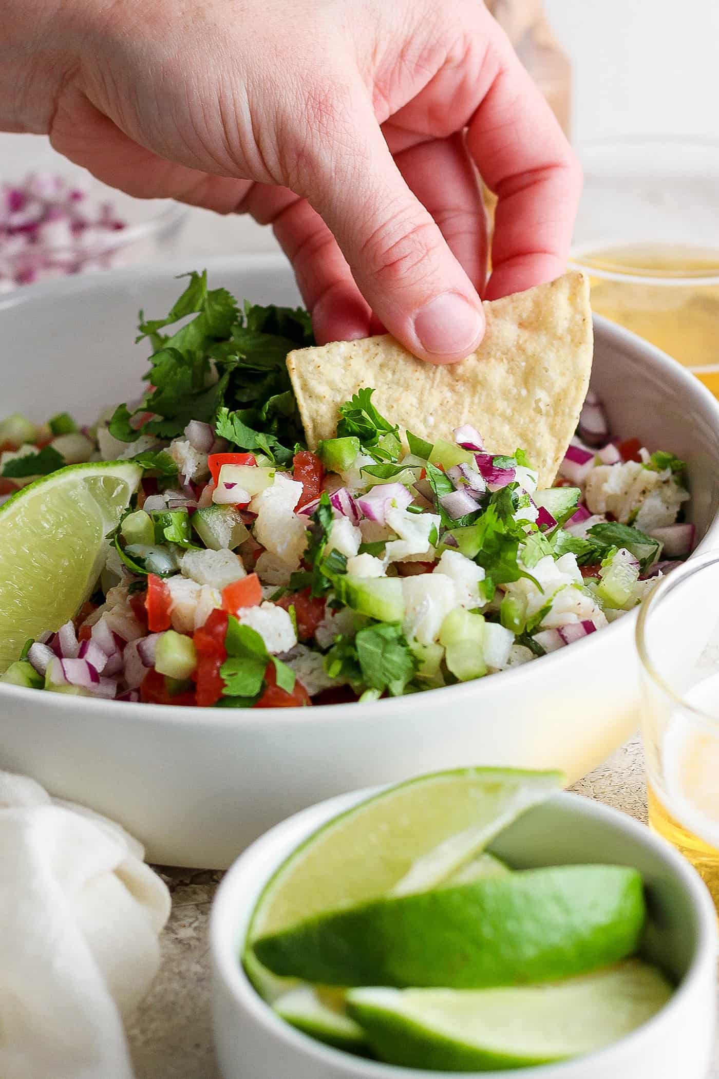 A hand dips a tortilla chip into a bowl of classic ceviche.