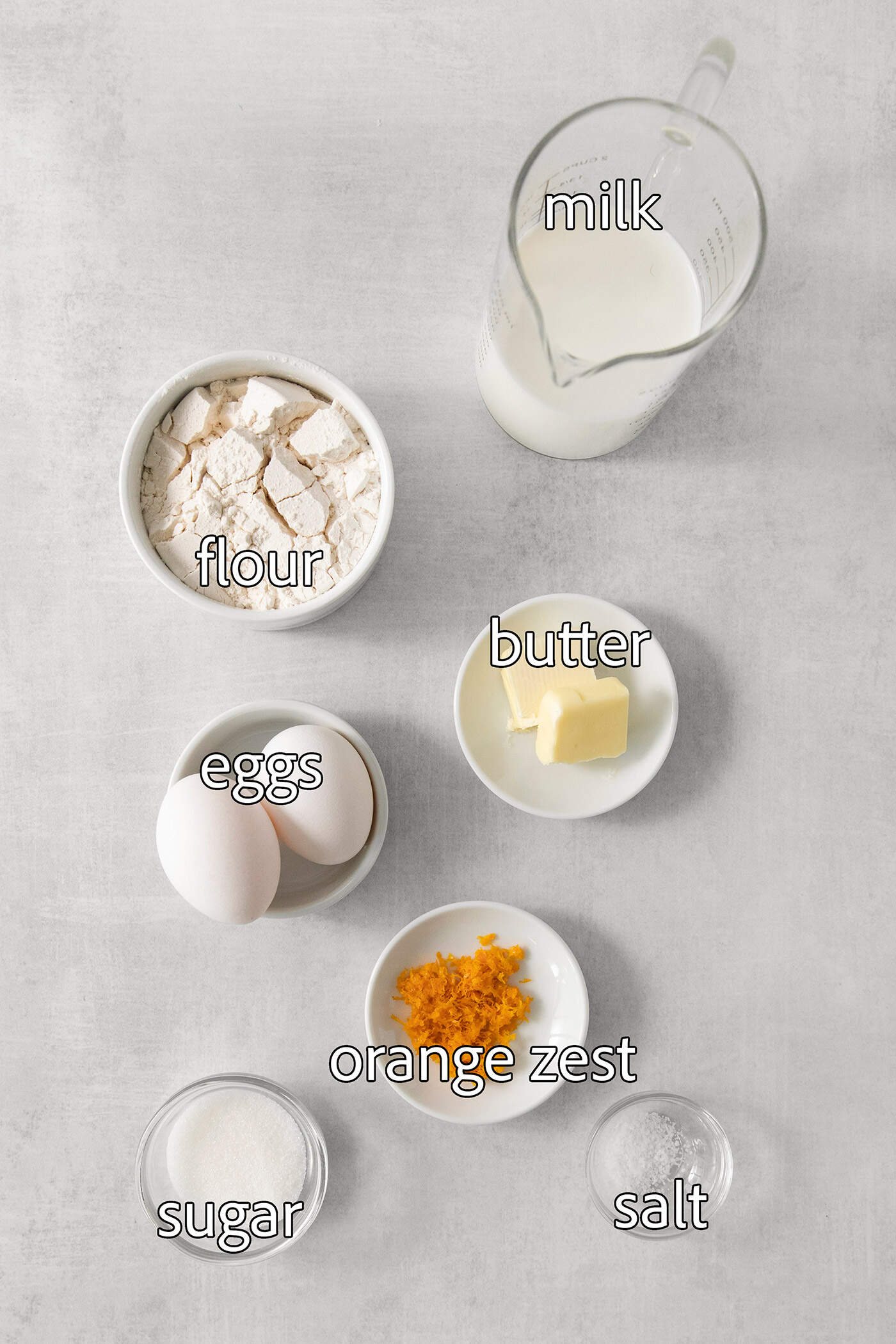 The ingredients for crepes Suzette are shown labeled and portioned out: orange zest, eggs, flour, butter, milk.