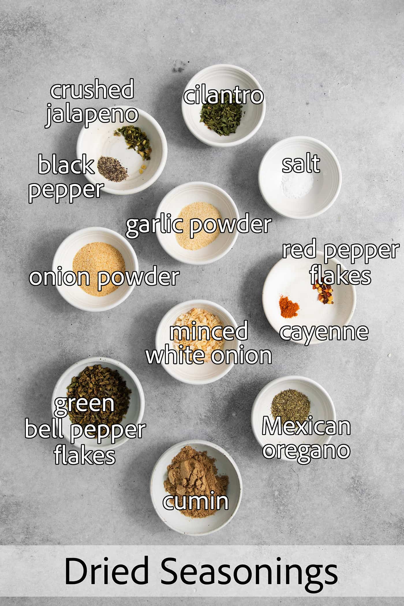 All of the spices needed for green taco seasoning are shown labelled and portioned out: onion and garlic powder, dried onion, salt and pepper, dried peppers, dried cilantro.