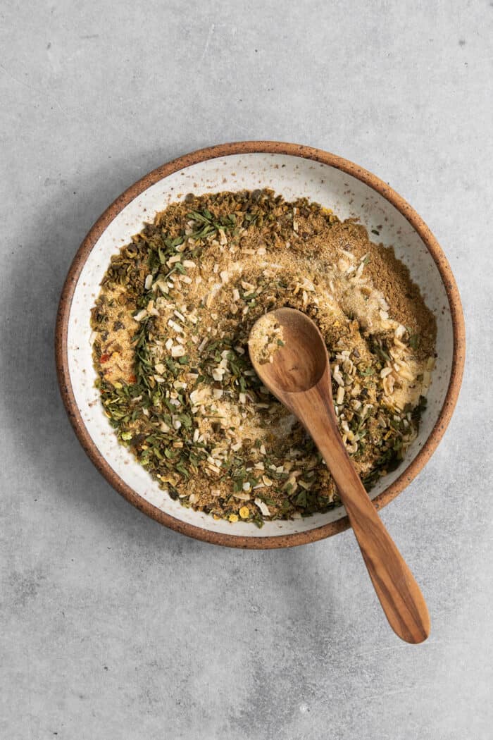 A wooden spoon stirs a bowl of spices for green taco seasoning.