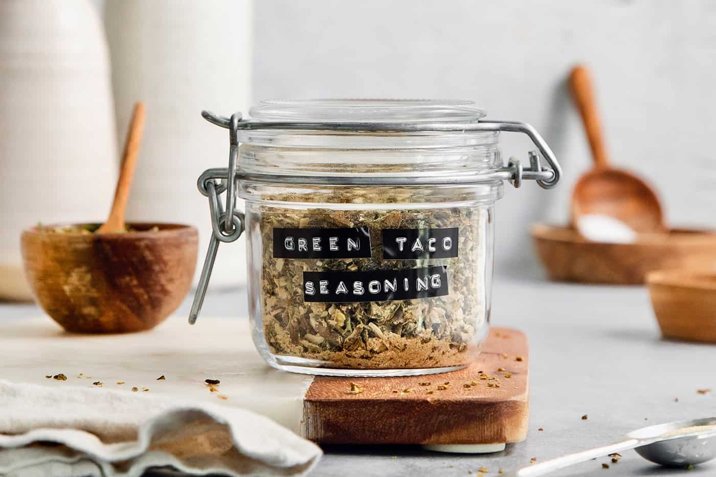 A labeled glass jar of green taco seasoning on a cutting board.