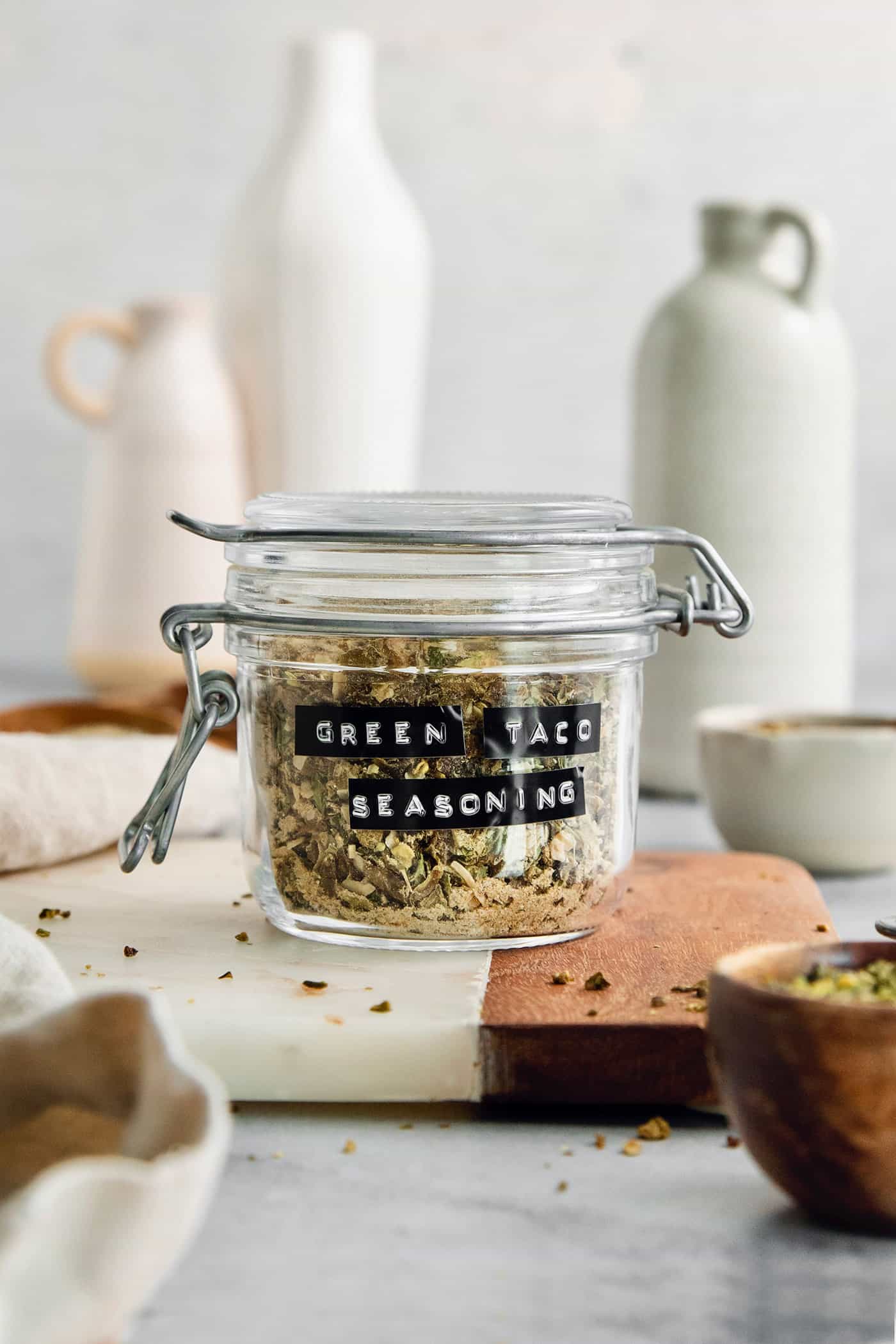 A labeled glass jar of green taco seasoning on a cutting board.