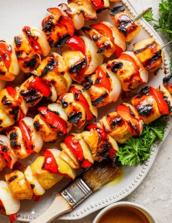A serving platter of honey mustard chicken kabobs on skewers.