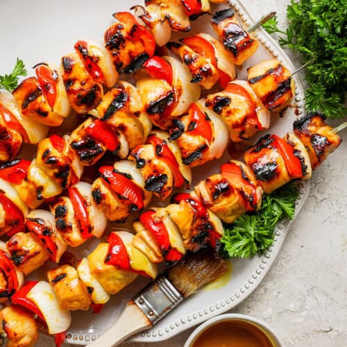 A serving platter of honey mustard chicken kabobs on skewers.