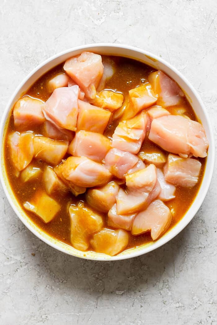 Chicken pieces marinate in a bowl for honey mustard chicken kabobs.