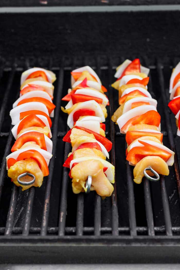 Chicken skewers cook on a grill.