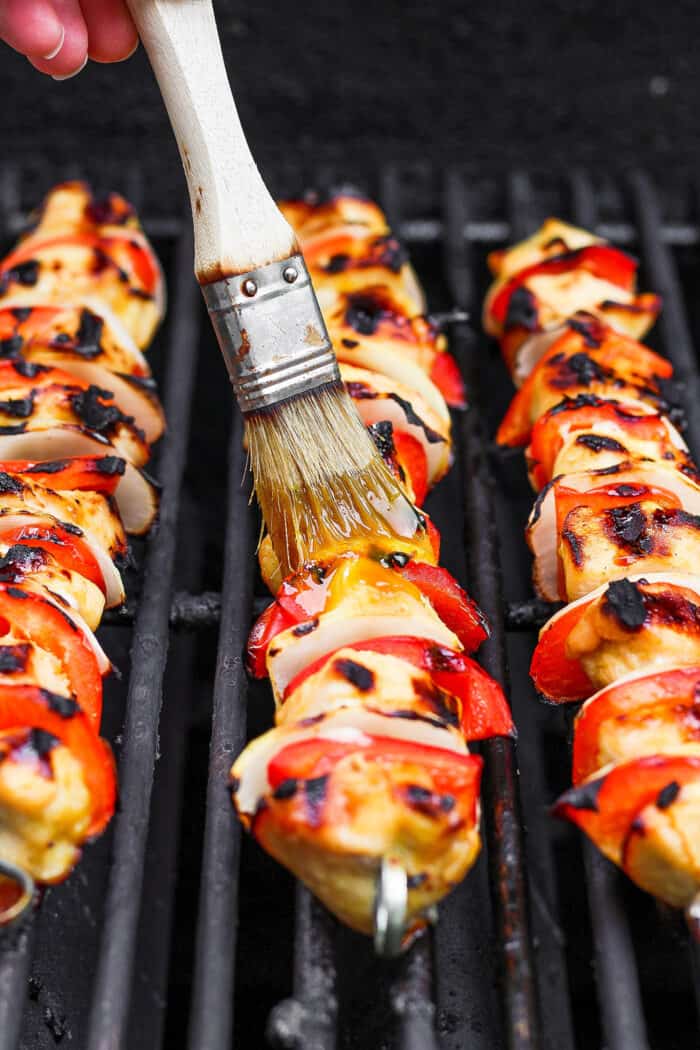 A brush brushes sauce onto skewers of chicken.