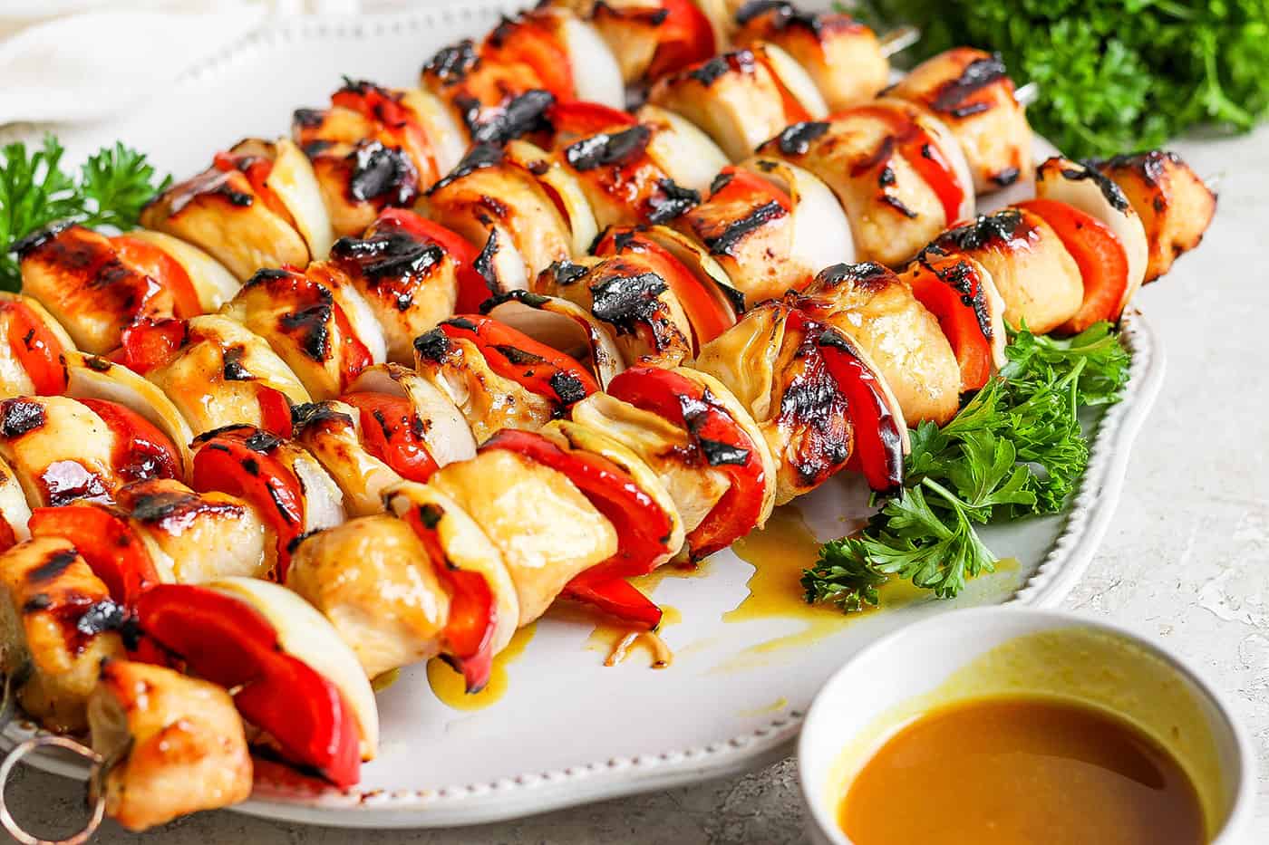 Honey mustard chicken kabobs on a plate next to a bowl of sauce.