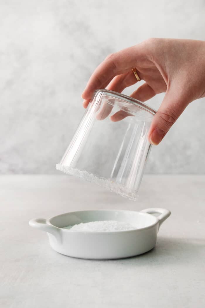 A hand dips a glass into a dish of salt.