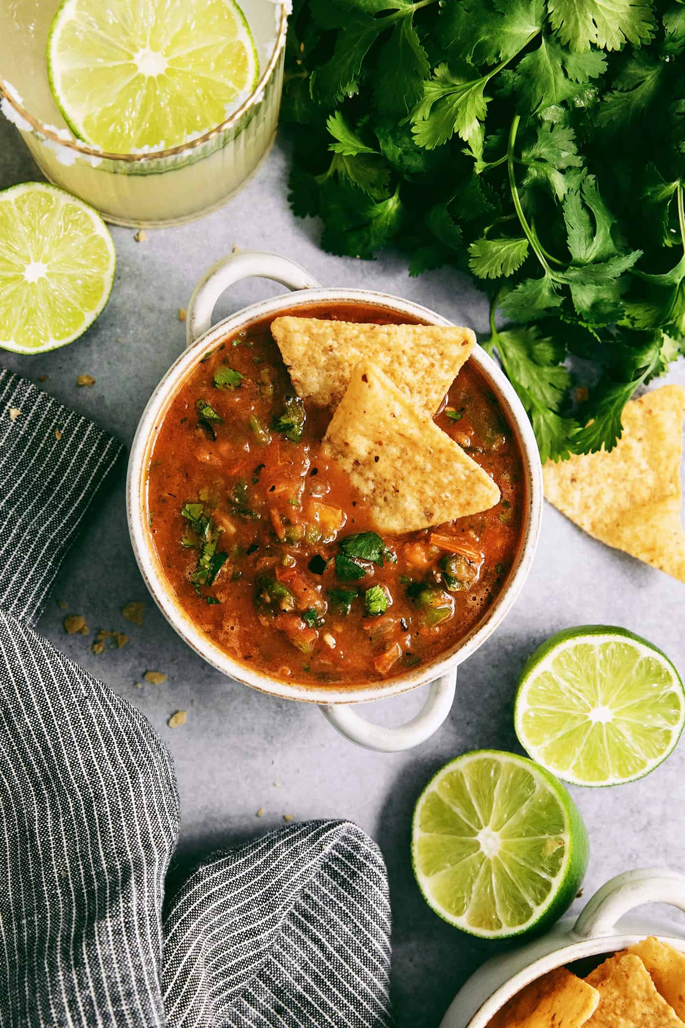 A white bowl of warm salsa topped with tortilla chips.