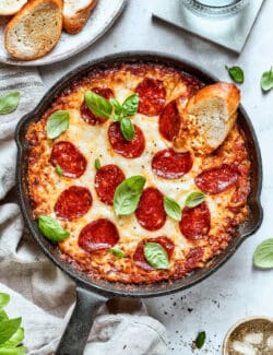 A slice of bread is dipped into a pan of pizza dip.