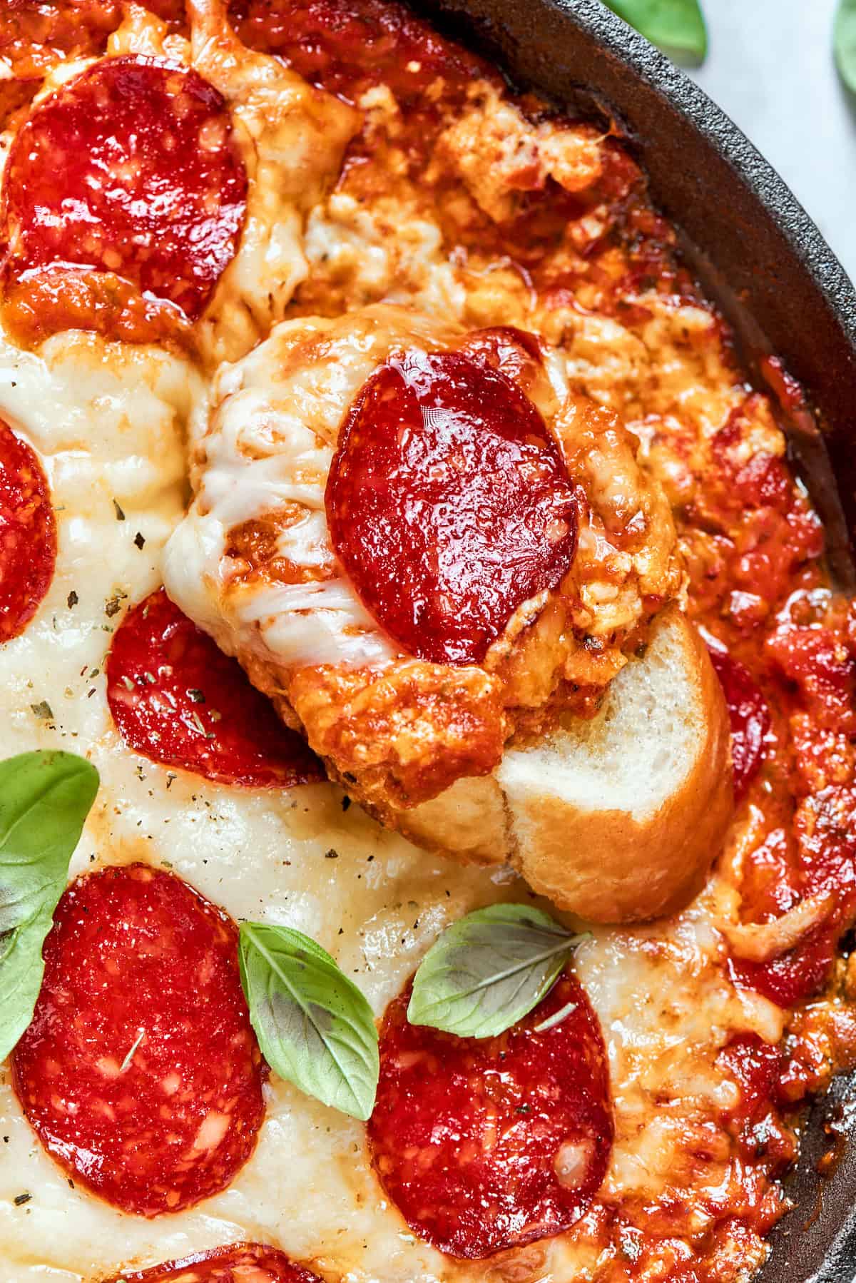A piece of bread topped with pizza dip and a slice of pepperoni on top of a pan of dip.