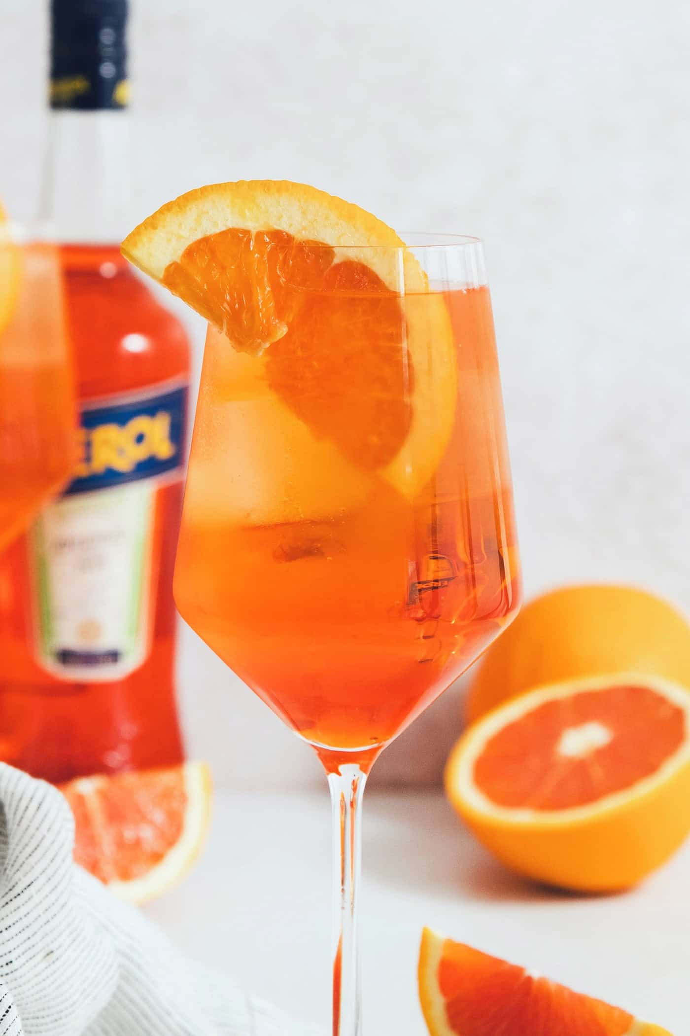 An orange wedge garnishes a wine glass of Aperol spritz.