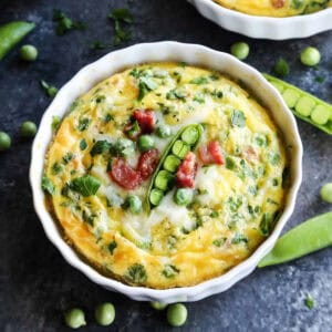 A ramekin of baked eggs is topped with peas.