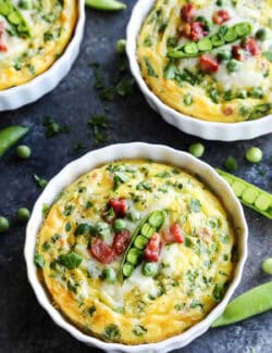 Three ramekins of baked eggs are topped with peas.