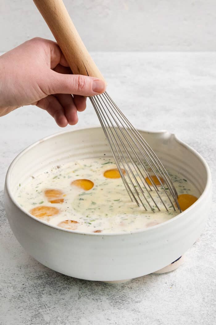 Eggs are whisked with cream in a bowl for baked eggs.