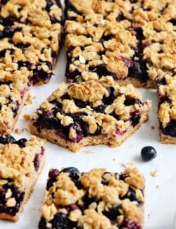A batch of blueberry crumble bars, the one in the middle has a bite taken out.